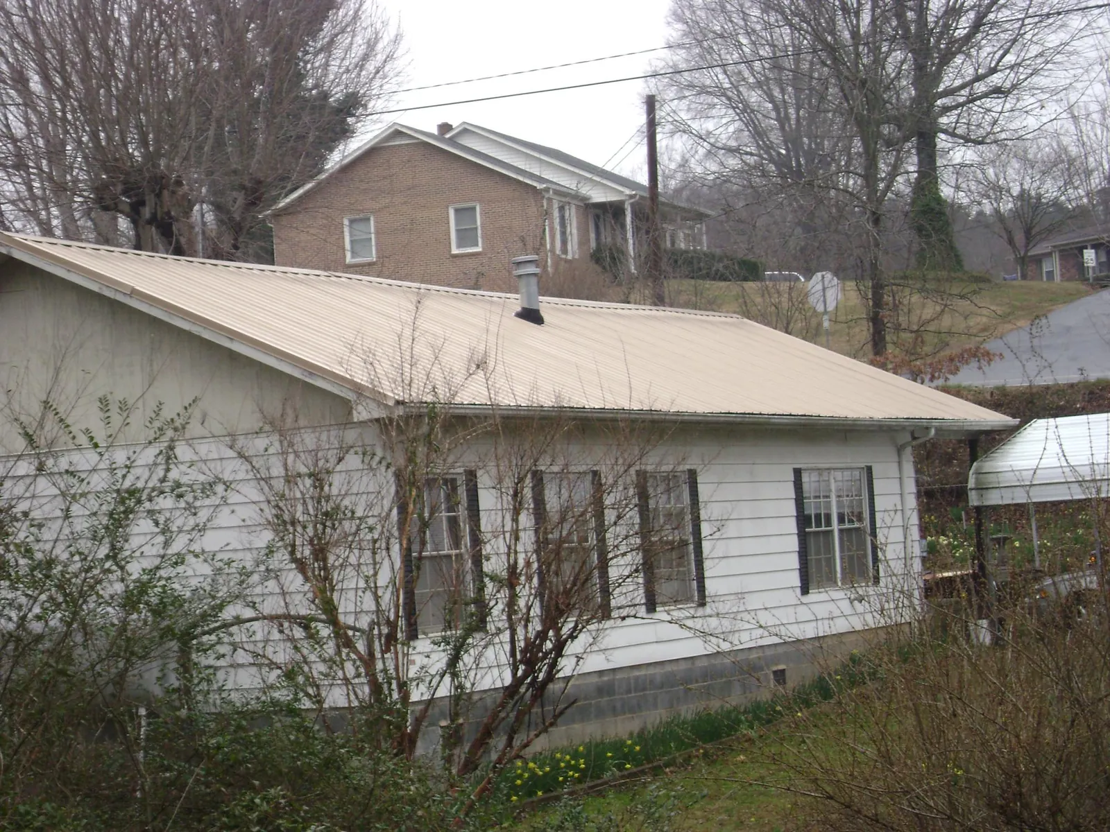 Tan metal roof on a white sided house set into a hillside — Commercial Roofing by Roofing Brothers in Riverside